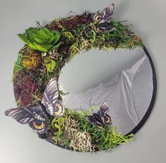 a circular mirror with grass and butterflies on the front, surrounded by succulents