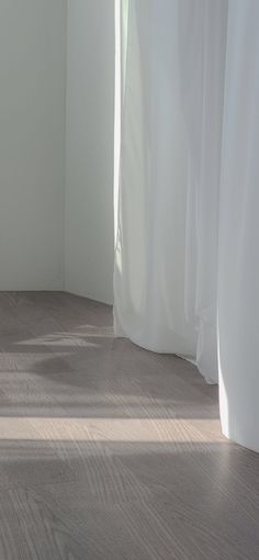 an empty room with white curtains and wood flooring