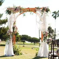 an outdoor wedding setup with white draping and pink flowers on the arbors