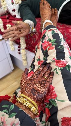 two people with henna tattoos on their hands sitting in front of a bed covered in red and white flowers