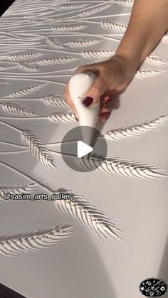 a person is using an object to paint the surface of a wall with white feathers on it