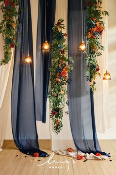 an arrangement of flowers and greenery is hanging from the ceiling in front of curtains