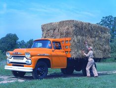 an orange truck with hay bales in the back and a man standing next to it