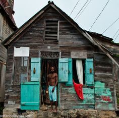 a man is standing in the doorway of an old wooden house with blue shutters