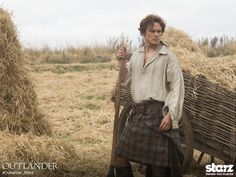 a man in a kilt holding a stick and standing next to a pile of hay