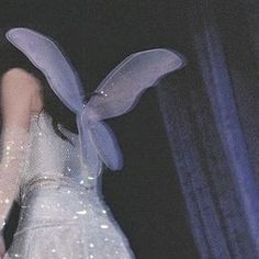 a woman in a white dress with blue wings on her head and hands behind her back