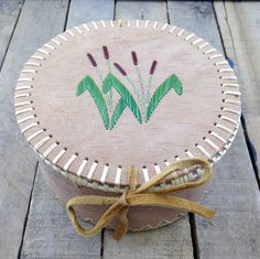 a round wooden box with designs on the lid and ribbon tied around it's edge