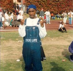 a man standing in the grass with his hands up and wearing overalls that say tug life