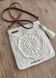 a white crocheted bag sitting on top of a wooden floor next to a brown leather strap