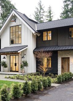 a large white house with black trim and windows on the front, surrounded by greenery