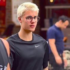 a young man with glasses is standing in front of two other men wearing black shirts