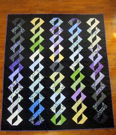 a black quilt with multicolored strips on it sitting on top of a wooden floor