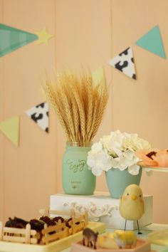 a table topped with cakes and flowers on top of a wooden table covered in bunting