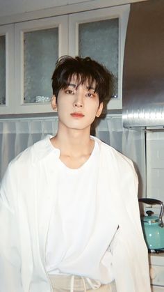 a young man standing in front of a stove top oven wearing a white shirt and khaki pants