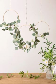 two wreaths with flowers hanging from them on a table next to a vase filled with greenery