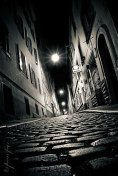 an empty cobblestone street at night with the light shining on it's windows