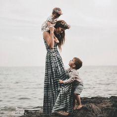 a woman holding a child while standing on top of a rock next to the ocean