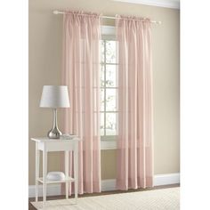 pink curtains hanging in front of a window with a lamp on the table next to it