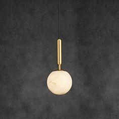 a white marble ball hanging from a brass colored light fixture on a black wall background