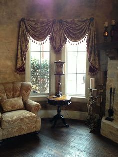 a living room with two chairs and a table in front of a window that has curtains on the windowsill