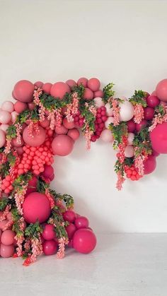 an arrangement of pink and red balloons hanging from the ceiling in front of a white wall