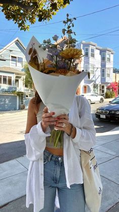 a woman holding a bouquet of flowers in her hands while standing on the side walk