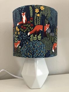 a lampshade with foxes and flowers on it, sitting on a white table