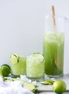 two glasses filled with cucumber and limeade on a table next to other drinks