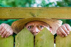 an old man wearing a straw hat peeking over a wooden fence