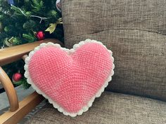 a pink knitted heart pillow sitting on a chair next to a christmas tree in a living room