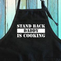 a black apron with the words stand back daddy is cooking printed on it in white