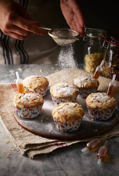 a person sprinkling sugar onto some muffins on top of a plate