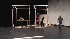 three people standing in front of a wooden structure on a stage with ladders and scaffolding