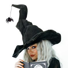 a woman wearing a witches hat and holding a book with a spider hanging from it