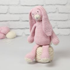 a crocheted pink bunny sitting on top of a ball of yarn