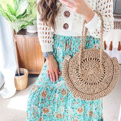 a woman holding a cell phone while wearing a blue skirt and white sweater with flowers on it