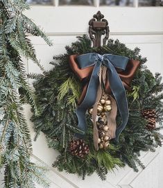 a wreath hanging on the side of a door decorated with pine cones, bells and ribbon