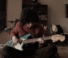 a woman sitting on the floor playing an electric guitar