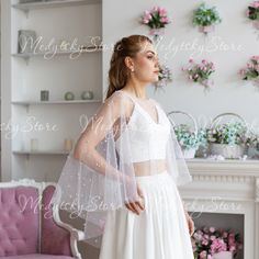 a woman standing in front of a fireplace wearing a white wedding dress with sheer sleeves