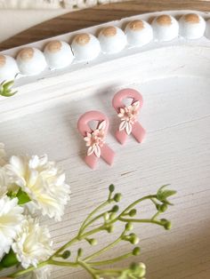 two pink earrings sitting on top of a white tray next to some flowers and eggs