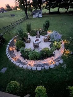 an outdoor fire pit surrounded by rocks and plants in the middle of a yard at dusk