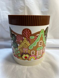 a ceramic cup with gingerbread houses on the front and brown trim around the bottom