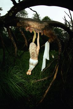 a woman hanging from a tree branch in the grass with her shirt pulled up to her chest