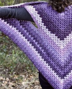 a woman wearing a purple and white crocheted shawl in front of trees