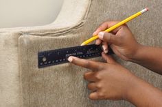 a person holding a ruler and pencil in their hand while pointing to it on the couch