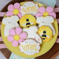 decorated cookies on a yellow plate with pink and white flowers in the shape of bees