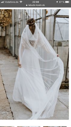 a woman in a white dress and veil is walking down the street with her back to the camera