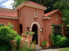 an orange house with red tile roofing and green plants in front of the building