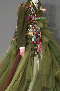 a woman in a green dress with lots of buttons on her jacket and skirt is walking down the runway