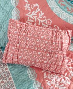 a pink and blue bed with pillows on top of it, next to an orange pillow